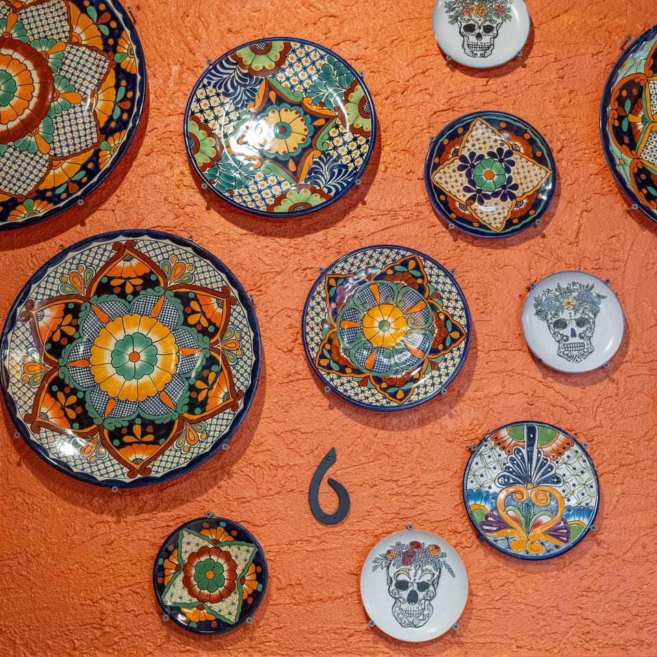 Colorful hand-painted ceramic plates and skull artwork arranged on a textured terracotta-orange wall.