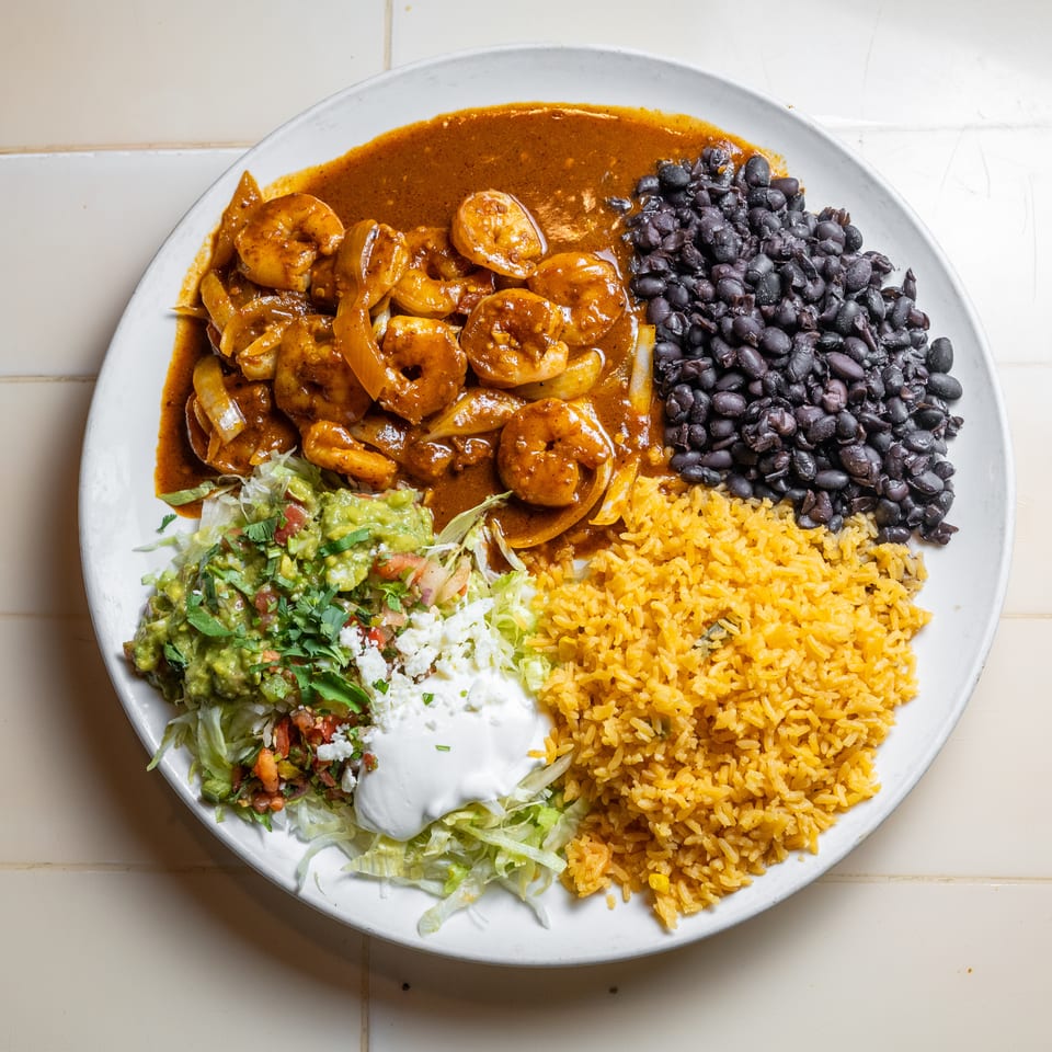 Plate of saucy shrimp, black beans, yellow rice, guacamole, pico de gallo, lettuce, cheese, and sour cream.