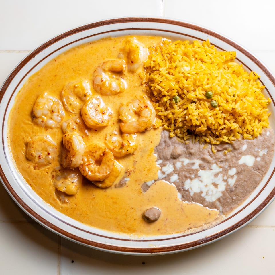 Plate of shrimp in creamy orange sauce with yellow rice, refried beans, and melted cheese.