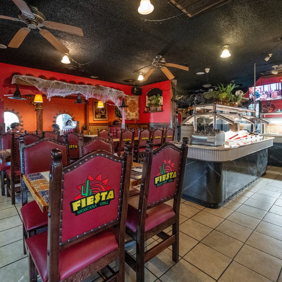 Fiesta Mexican Grill dining room with burgundy logo chairs, red walls, ceiling fans, festive décor, and a buffet counter.