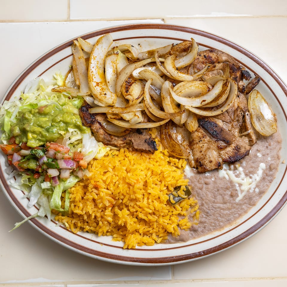 Mexican plate with grilled meat and onions, yellow rice, refried beans, guacamole, lettuce, and pico de gallo.