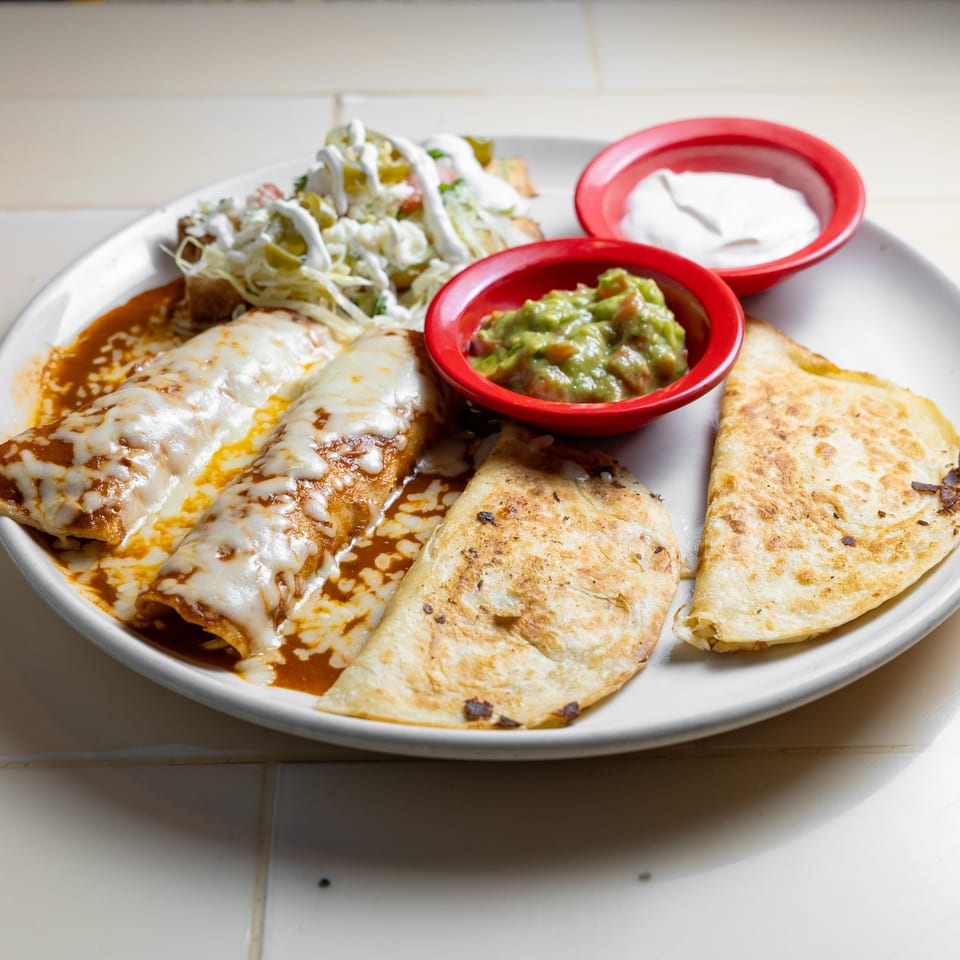 Mexican platter featuring cheese-covered enchiladas, grilled quesadillas, shredded lettuce salad, guacamole, and sour cream.