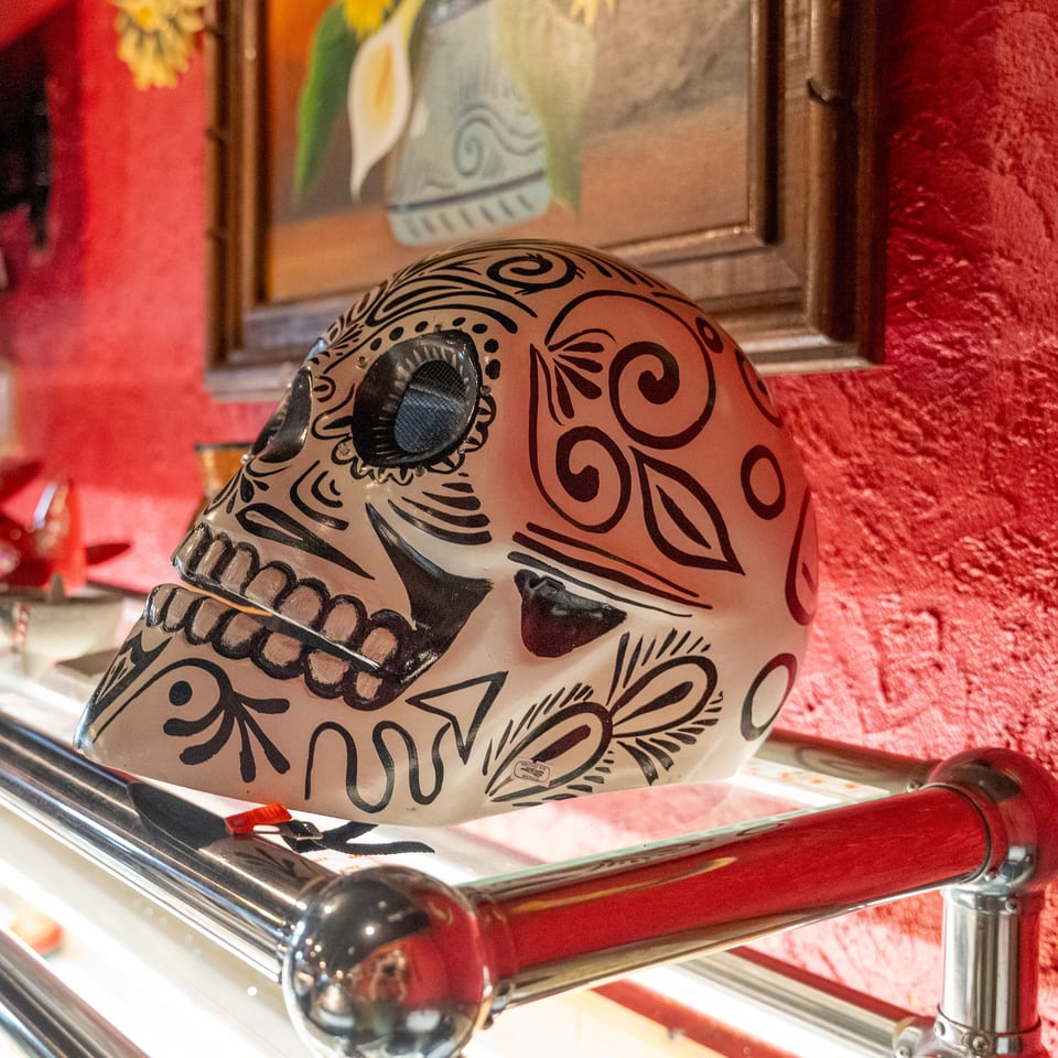 Decorative ceramic sugar skull with black floral patterns displayed against a red restaurant wall.