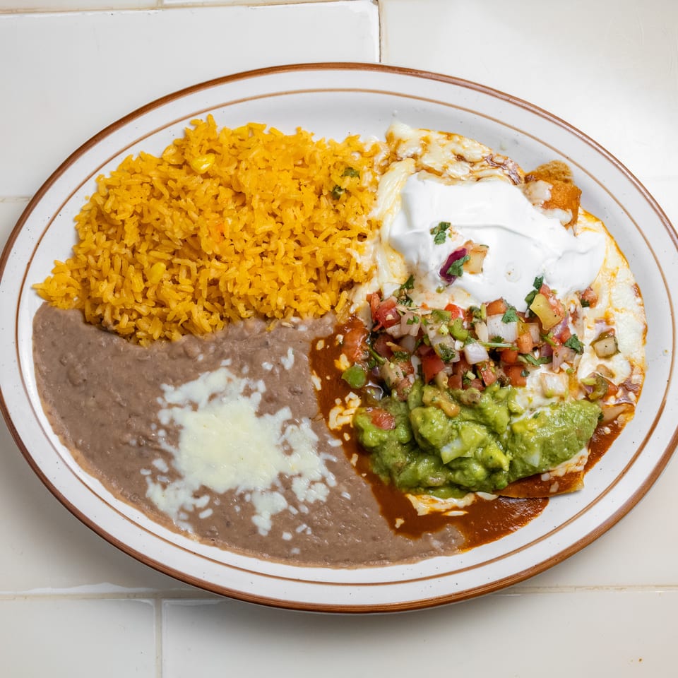 Mexican plate with yellow rice, refried beans, a fried egg topped with sour cream, pico de gallo, and guacamole.