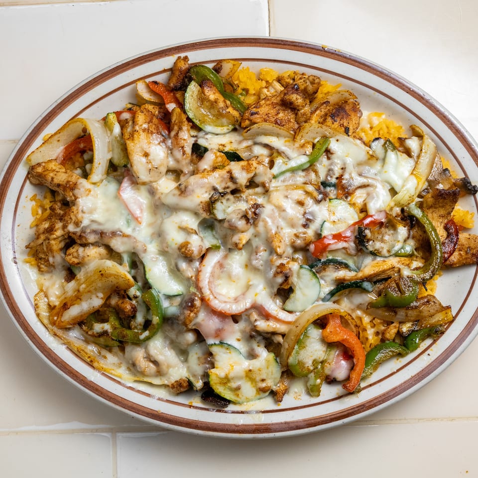 Oval platter of grilled chicken, peppers, onions, zucchini, and melted cheese served over seasoned yellow rice.