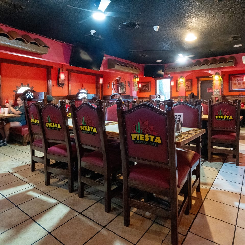 Colorful Fiesta Mexicana restaurant dining room with red walls, branded chairs, tiled floors, tables, and seated diners.