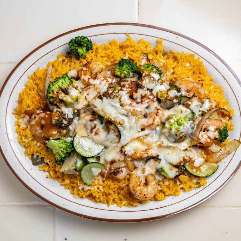 Oval platter of yellow rice topped with shrimp, grilled vegetables, and melted cheese.
