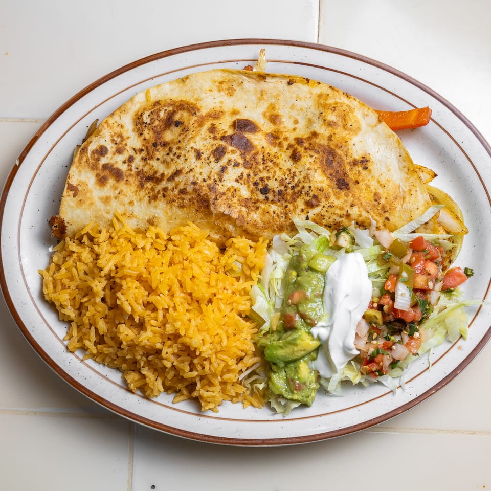 Plate of toasted stuffed flatbread with yellow rice, lettuce, guacamole, sour cream, and pico de gallo.