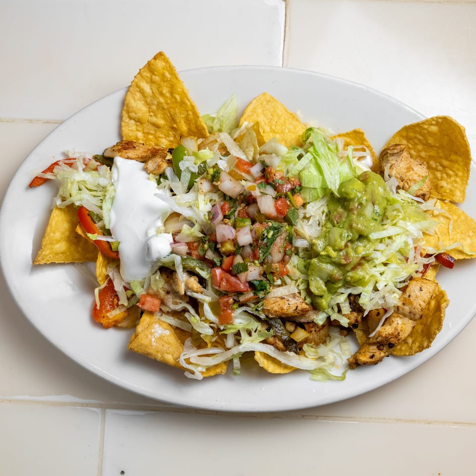 Plate of chicken nachos topped with shredded lettuce, sour cream, guacamole, pico de gallo, and cheese tortilla chips.