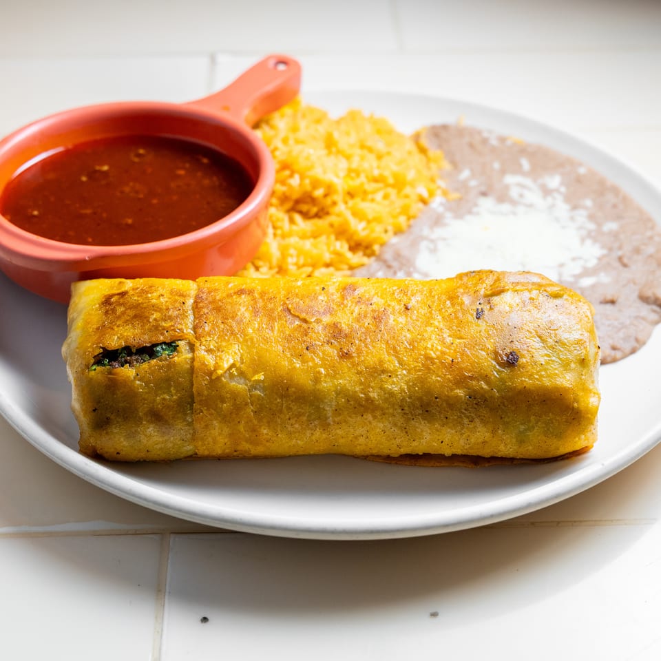 Golden-brown burrito served with Mexican rice, refried beans, and red salsa on a white plate.
