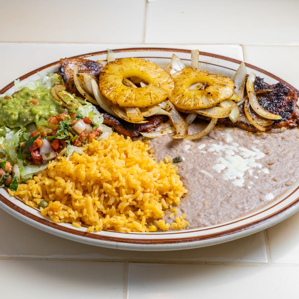 Mexican platter with grilled steak, pineapple and onions, yellow rice, refried beans, guacamole, and pico de gallo.