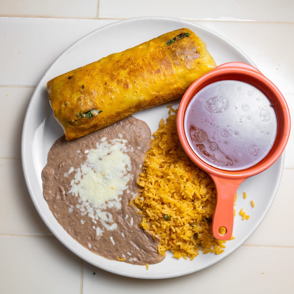 Plate of a golden stuffed enchilada with refried beans, Mexican rice, and a bowl of purple beverage.